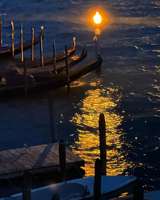 A glowing lamp illuminates gondolas and sends a golden reflection across dark water.