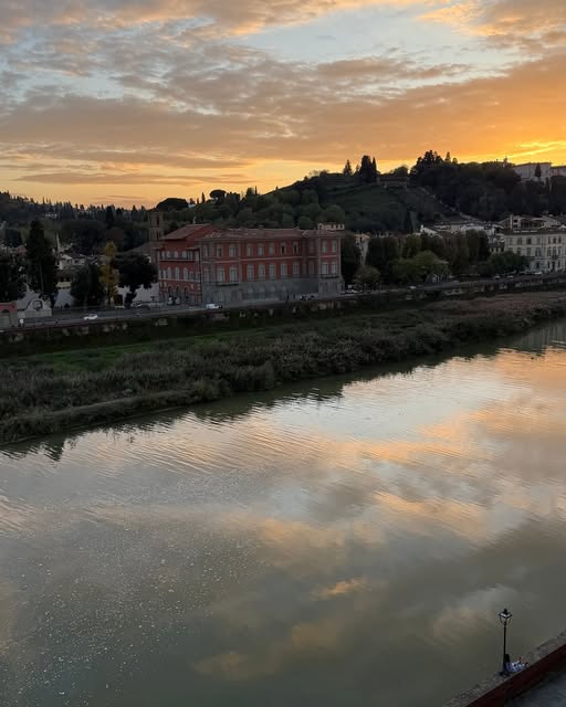 A warm evening sky and riverside buildings reflected in still water.